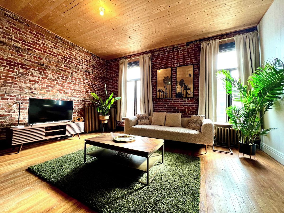 Una sala de estar con pared de ladrillo, televisor de pantalla plana, sofá, mesa de centro y una planta en maceta.