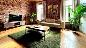 A living room with a brick wall, wooden ceiling, a flat-screen TV, a sofa, a coffee table, and potted plants.