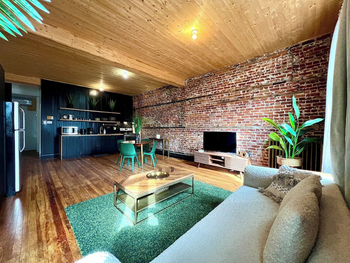 Una sala de estar moderna con pared de ladrillo, suelo de madera, un sofá, una mesa de centro y una televisión.