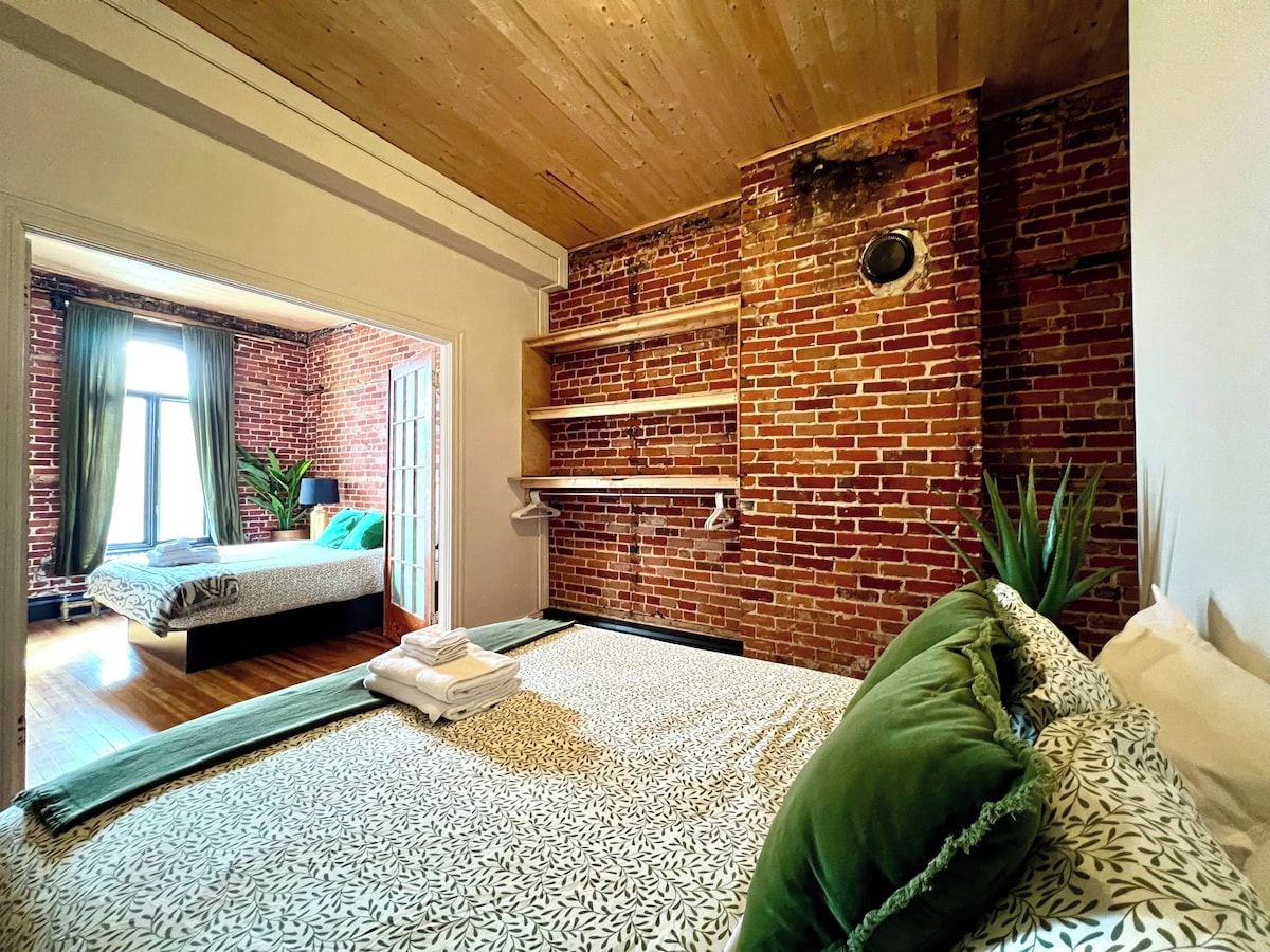 Quarto com parede de tijolos, uma cama, um sofá e teto de madeira.