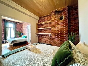 A room with a brick wall, a bed, a sofa, and a wooden ceiling.