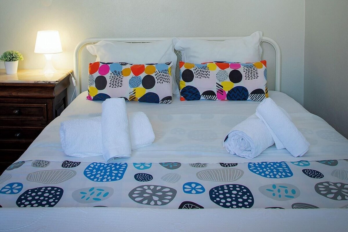 A neatly made bed with patterned bedding, a bedside lamp, and a painting on the wall.