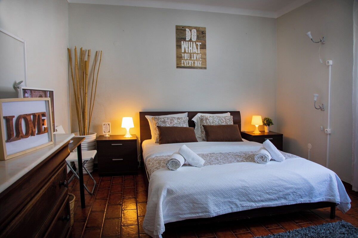 A neatly made bed with white linens, two bedside lamps, a wall-mounted sign, and a wooden floor.