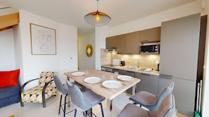 A modern kitchen with a dining area, including a table set for four, chairs, and a sofa with a geometric-patterned cushion.