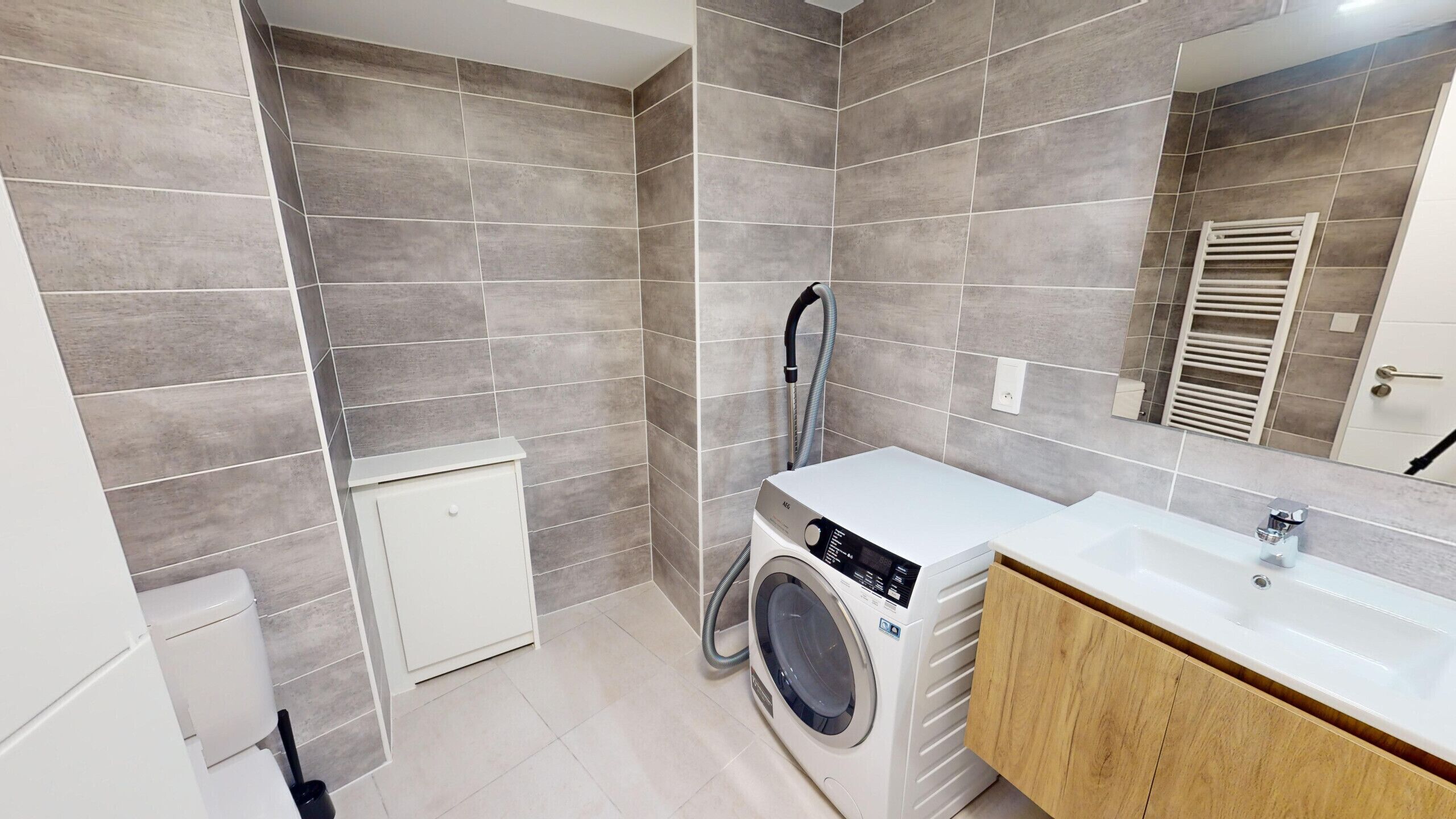 Un baño moderno con azulejos grises, lavadora, lavabo y espejo.