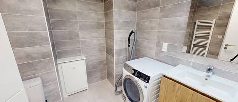 Un baño moderno con azulejos grises, lavadora, lavabo y espejo.