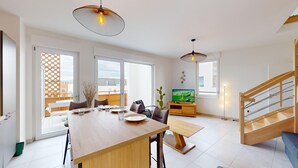 A spacious living area with a dining table, chairs, a TV, and a staircase.