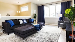 Een moderne woonkamer met een hoekbank, een salontafel en een groot raam met gordijnen.