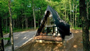 A modern, triangular wooden cabin with a glass facade, surrounded by a forest. - Fox Ridge-Black Alder Lodging (Logan)