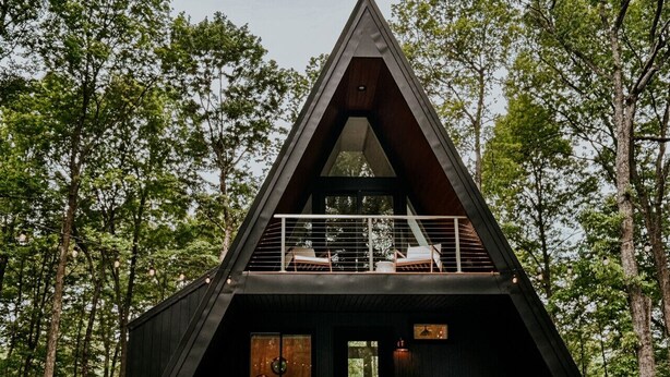 A modern, triangular-shaped cabin with a balcony, surrounded by trees. - Fox Ridge-Black Alder Lodging (Logan)