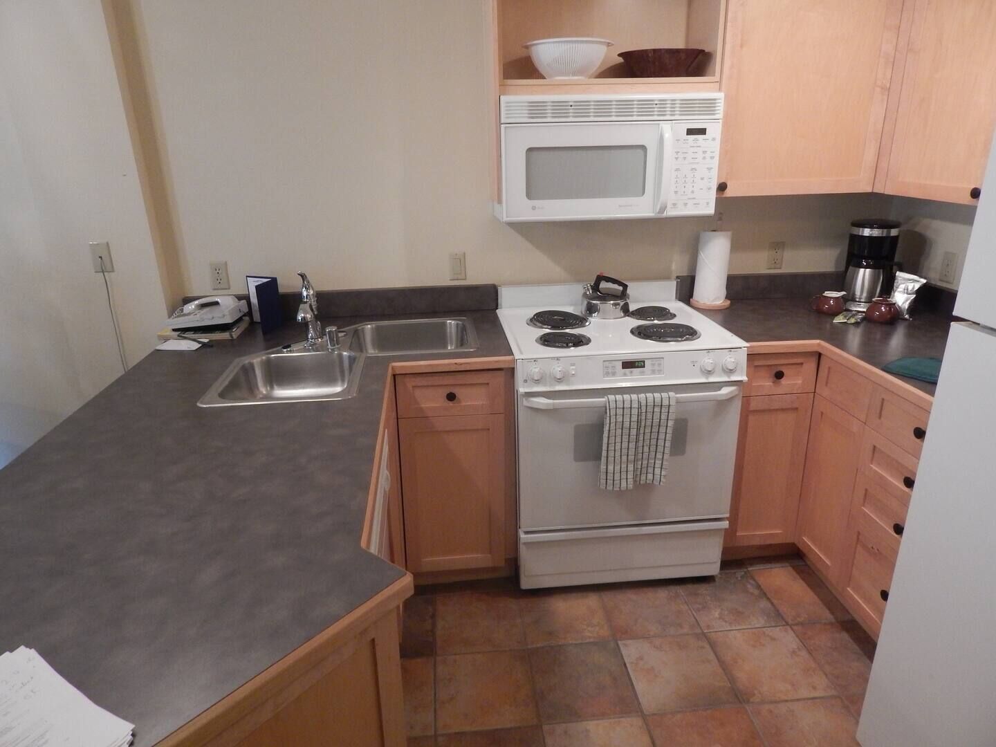 Cocina compacta con estufa, microondas, lavamanos y armarios de madera.
