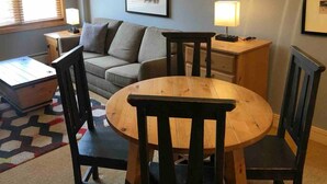 Un salon chaleureux avec une table ronde en bois, deux chaises, un canapé et une lampe posée sur une table d’appoint.