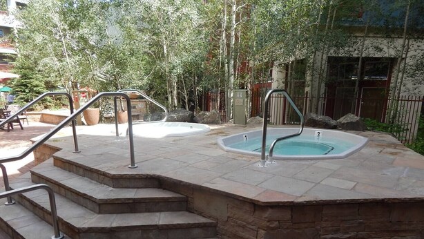 Une piscine en pierre, accessible par des marches, entourée d’une terrasse en briques et de rampes en métal.