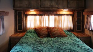 Un lit avec une couvre-lit à motifs, deux coussins décoratifs et une tête de lit dotée d’un éclairage intégré.