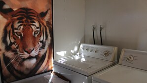 Un espace buanderie avec un lave-linge et un sèche-linge blancs, un mur blanc et un tableau représentant un tigre, encadré.