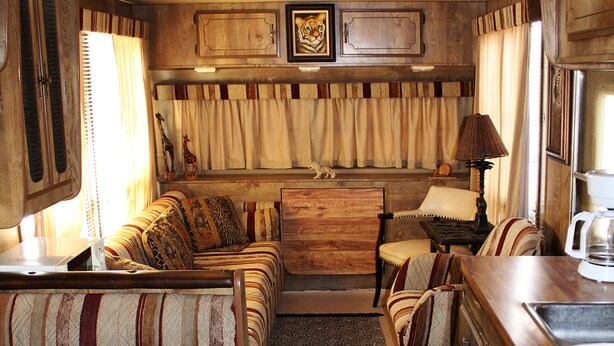 Un intérieur de camping-car compact comprenant un coin cuisine, un espace repas avec des coussins à rayures et un petit coin salon.