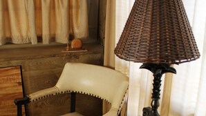 Une pièce comprenant une chaise en bois, une table avec une lampe et une étagère ornée d’un objet décoratif.