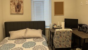 A bedroom with a bed, a desk, a chair, a window with blinds, a TV, and a fan. - Private Quaint Cozy Room (Denver)