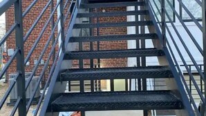 Un escalier en métal, doté d’une main courante, mène à l’entrée d’un bâtiment.