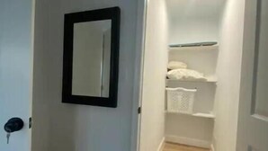 Un couloir étroit, doté d’un plancher en bois, mène à un placard équipé d’étagères et d’un panier suspendu.