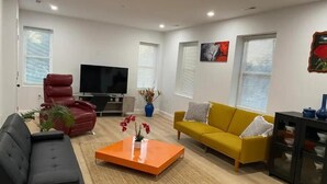 Un salon moderne avec un canapé noir, un canapé jaune, un fauteuil rouge et un téléviseur posé sur un meuble.