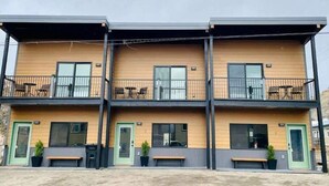 Un edifici modern de diversos pisos amb balcons, mobiliari exterior i teulada plana.