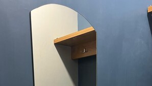 Un espejo con un estante de madera debajo, sujeto a una pared oscura.