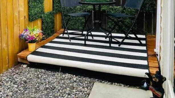 A small patio with a wooden fence, a black and white striped mat, two black chairs, and a small table.