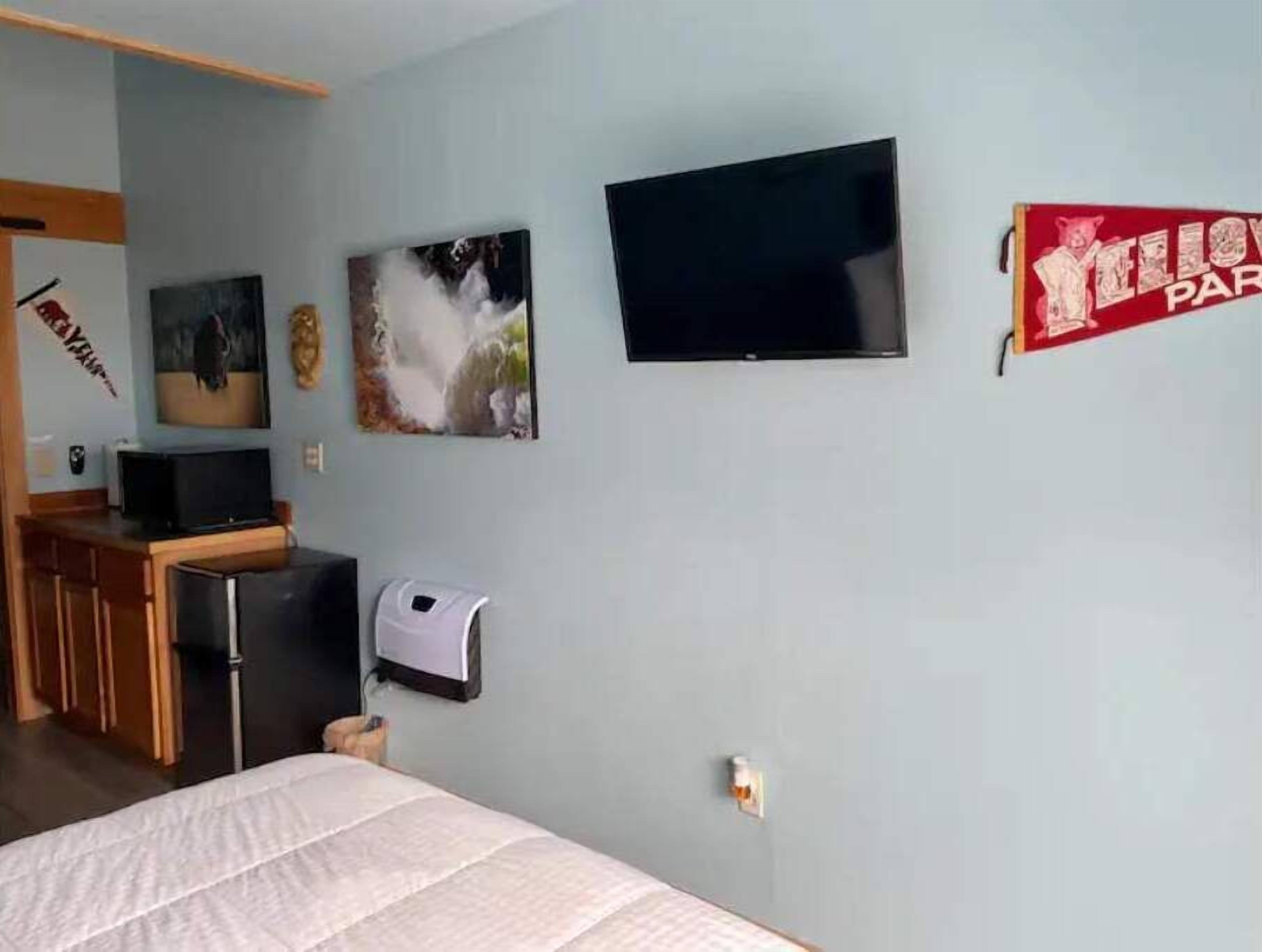 Ein Schlafzimmer mit einem Bett, einem an der Wand montierten Fernseher und einem kleinen Schreibtisch mit einem Computer.