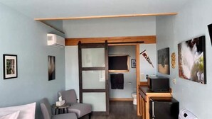 A compact hotel room with a bed, a seating area with a table, a kitchenette, and a TV.
