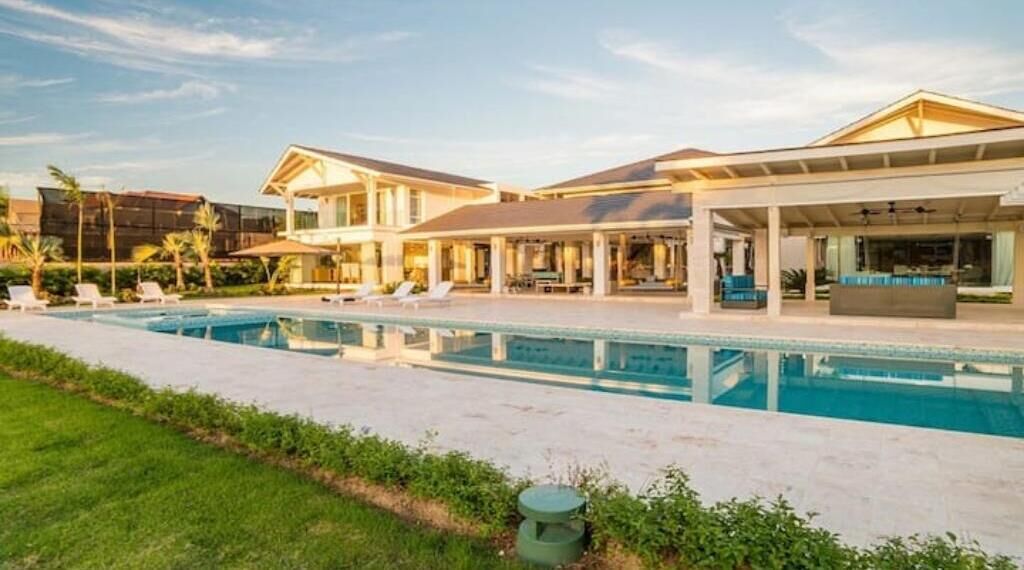 Un resort moderno con una gran piscina, un área de estar al aire libre techada y un césped bien cuidado.