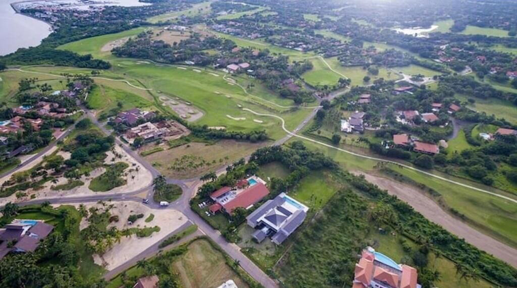 Vue aérienne d’un terrain de golf, avec des zones résidentielles, des routes et un grand bâtiment.