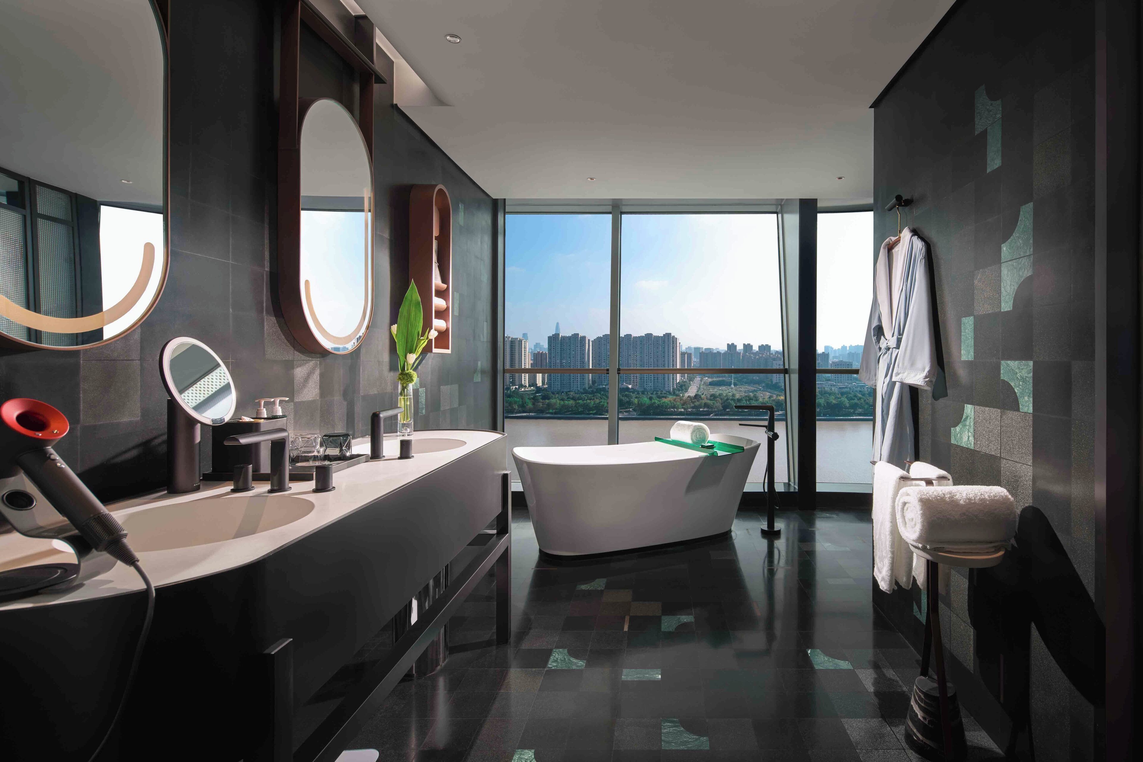 Un baño moderno con una bañera grande, lavamanos dobles y un amplio ventanal con vistas a la ciudad.