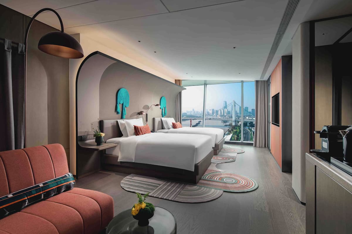 A modern hotel room with a large bed, a sofa, a coffee machine, and a city view.