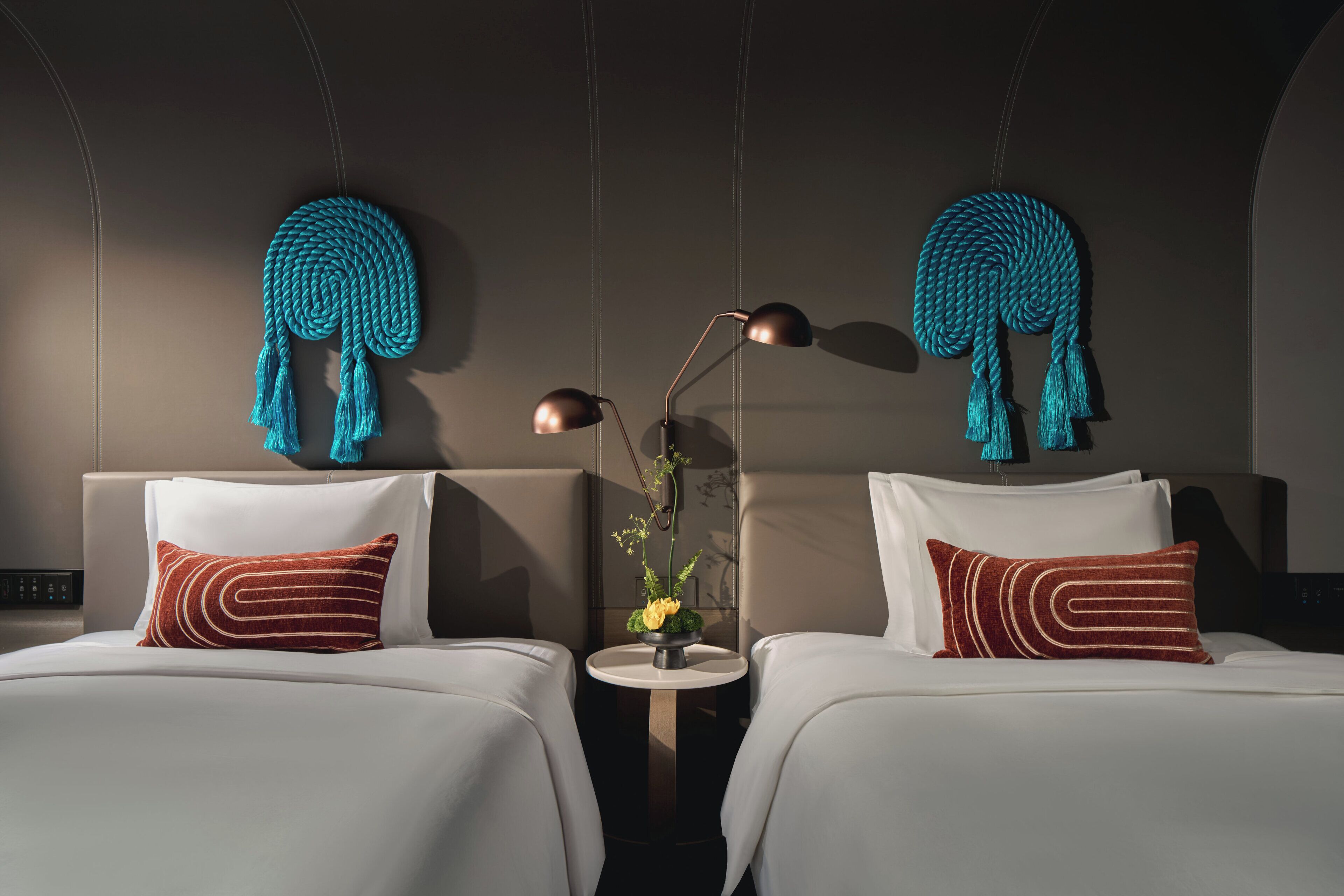 A hotel room with two beds, a small round table, and a wall-mounted lamp.