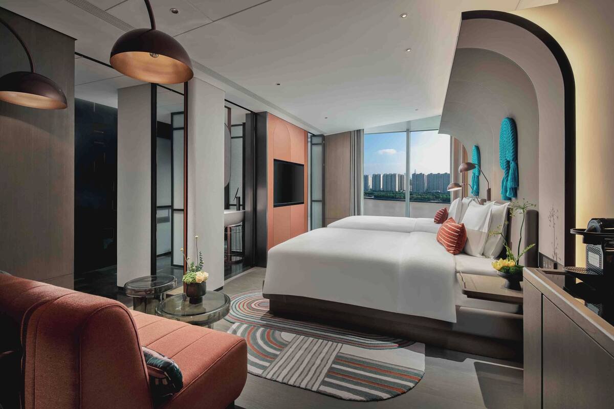 A modern hotel room with a large bed, a sofa, a TV, and a city view.