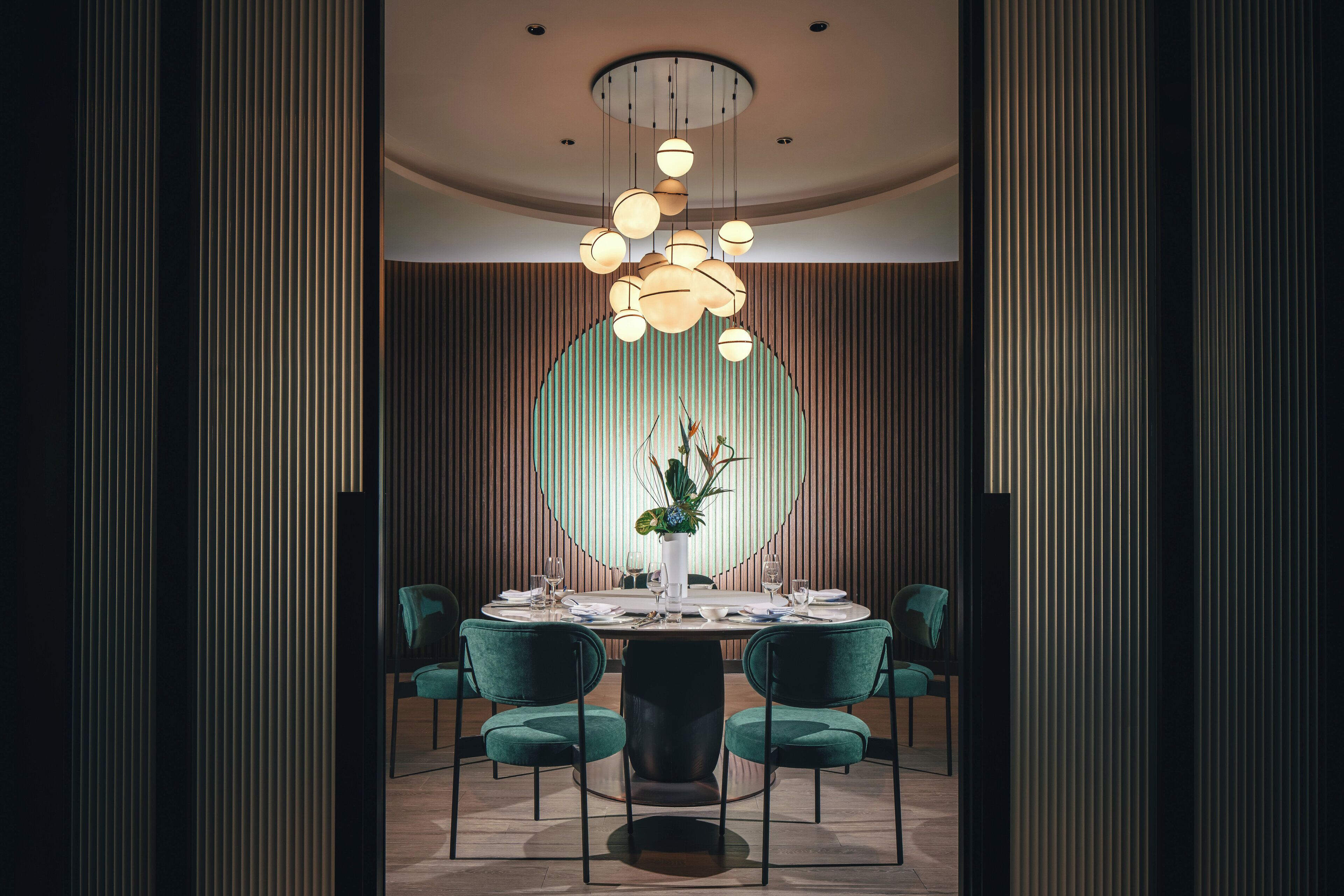 A modern dining area with a round table, teal chairs, and a central light fixture.