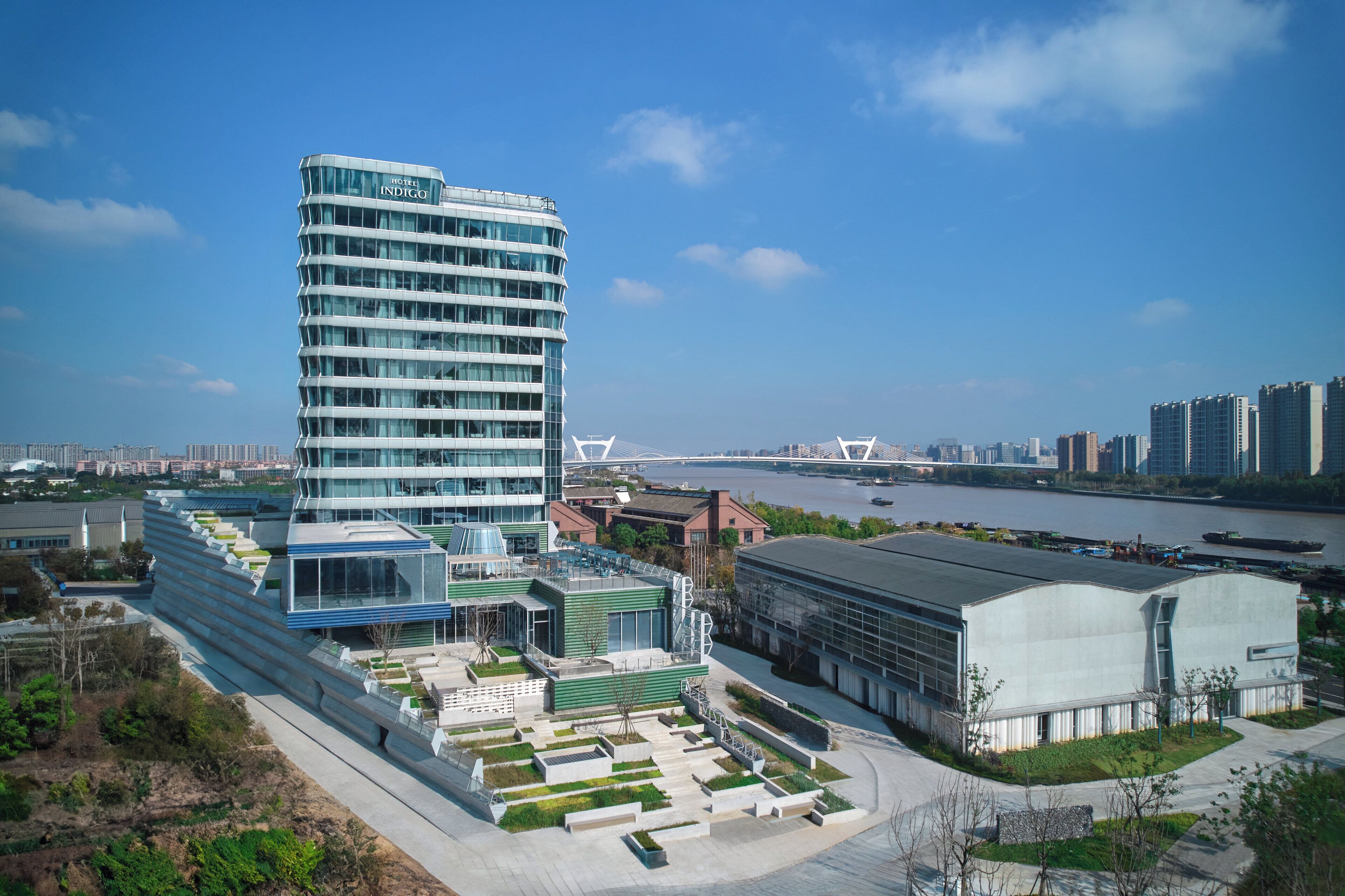 A modern building with a curved facade, a river in the background, and a bridge across the river.