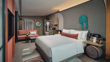 A modern hotel room with a large bed, a sofa, a desk with a lamp, and a TV.
