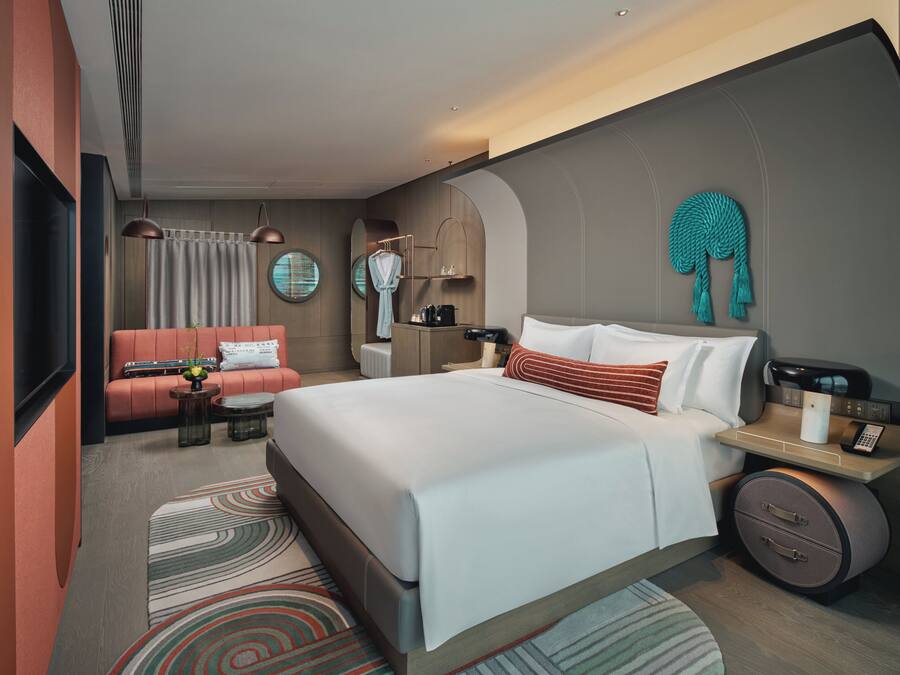A modern hotel room with a large bed, a sofa, a desk with a lamp, and a TV.
