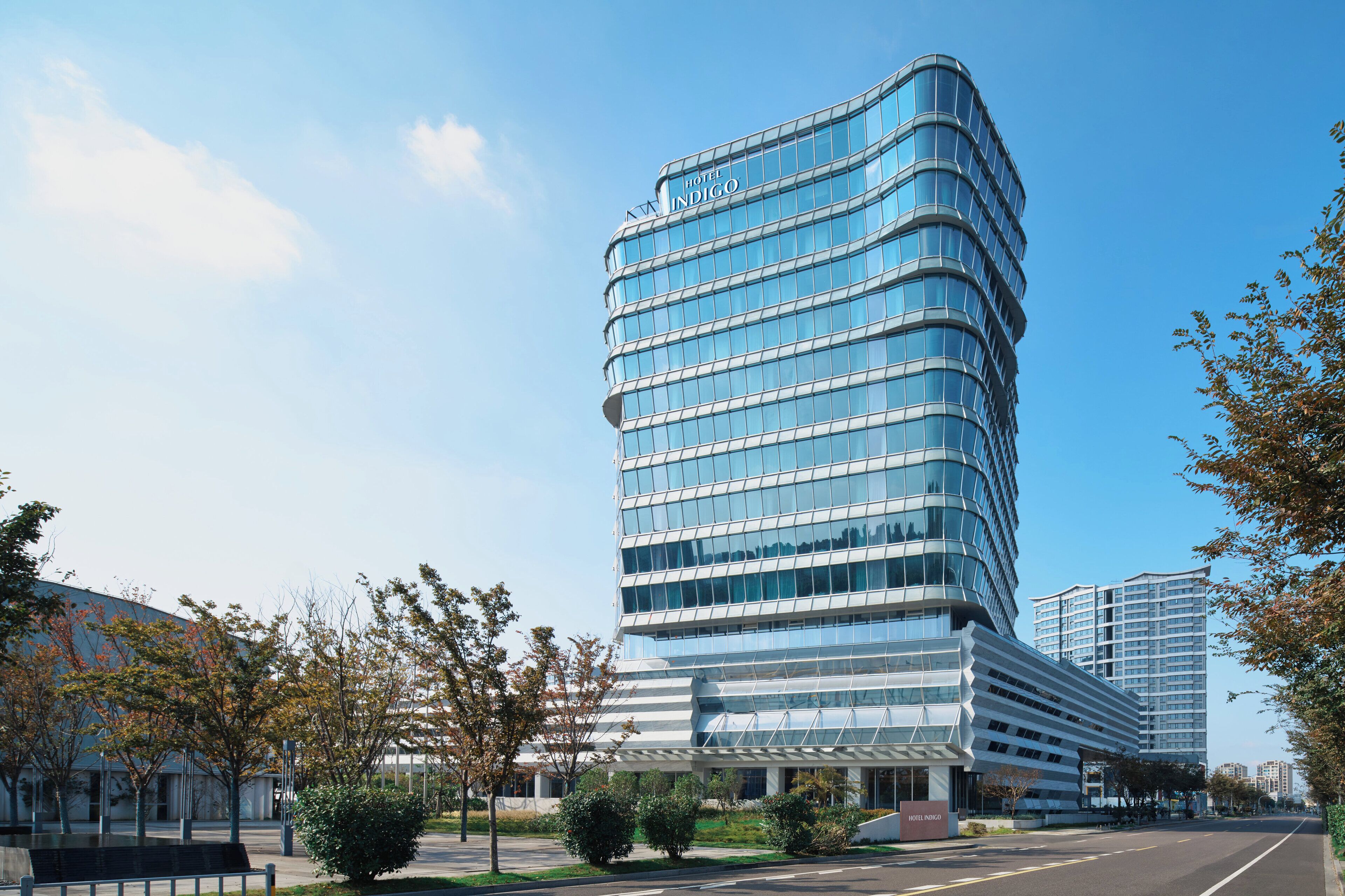 Un hotel moderno con facciata in vetro curvo, diversi piani e una ben visibile insegna con la scritta "Hotel Indigo".