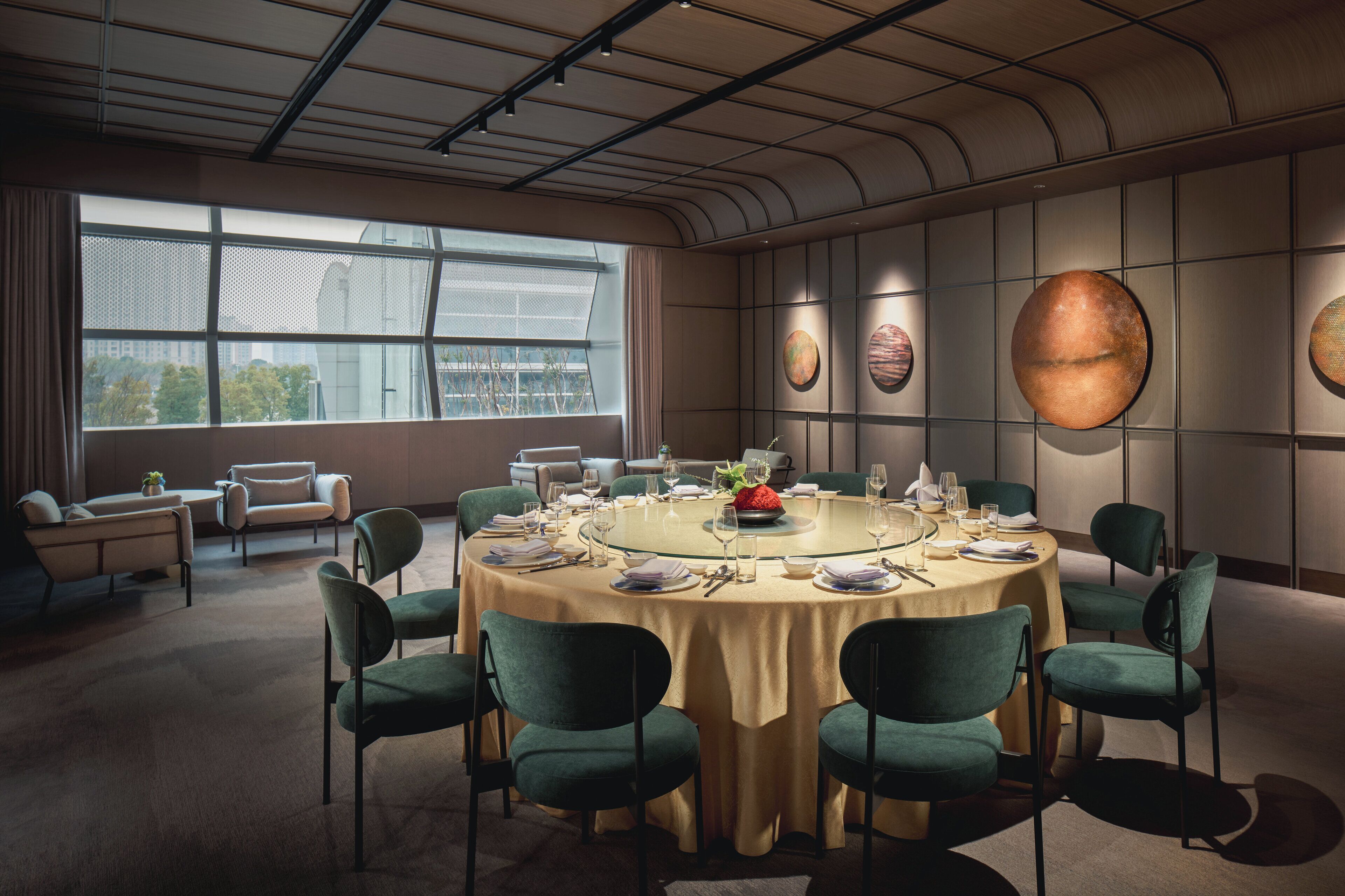 A modern dining room with a round table set for six, surrounded by green upholstered chairs.
