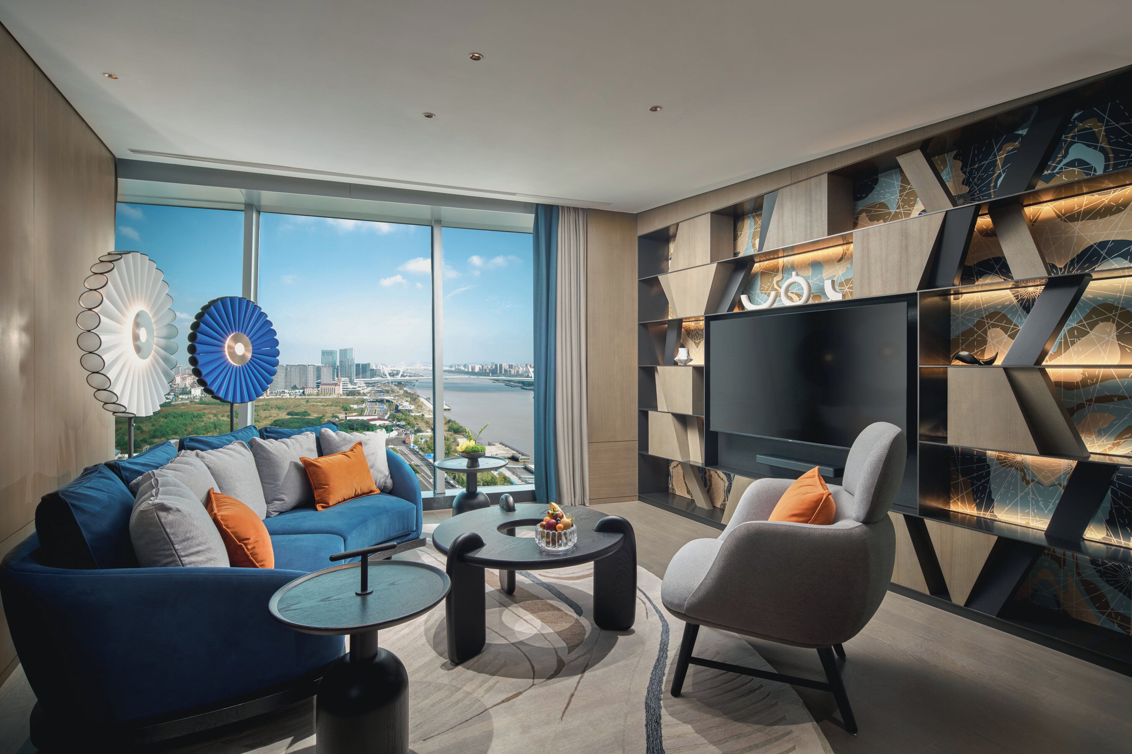 Una sala de estar moderna con un ventanal grande, un sofá azul, un sillón gris y un mueble para televisión.