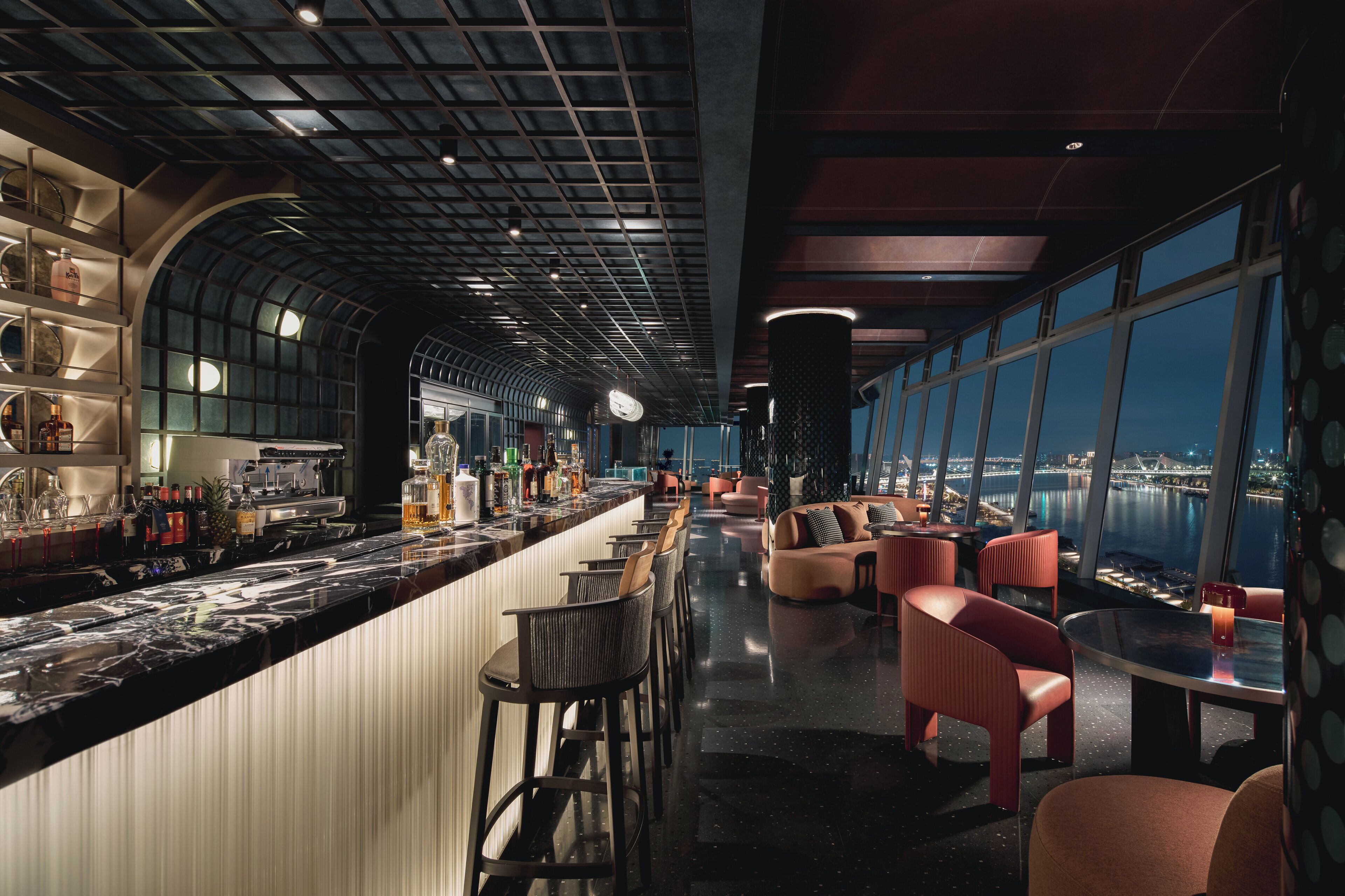 A modern bar area with a curved ceiling, bar stools, and a seating area with sofas and chairs.