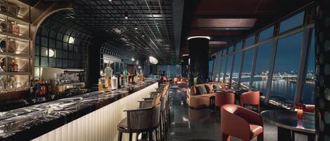 A modern bar area with a curved ceiling, bar stools, and a seating area with sofas and chairs.