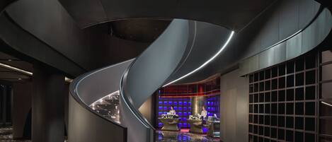 A modern interior with a curved staircase, a bar area, and a grid-patterned wall.