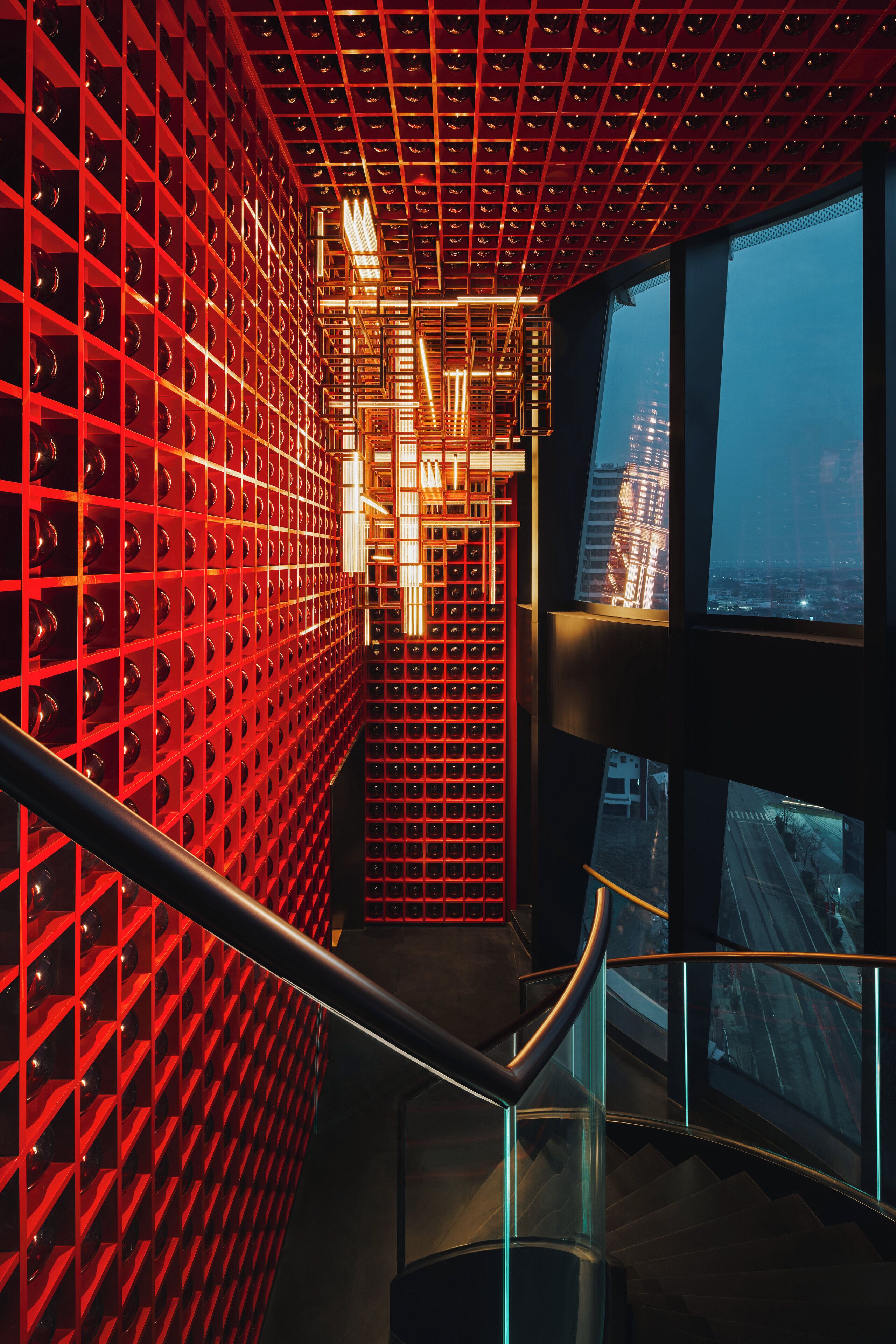 Un intérieur moderne avec un mur en briques rouges, un escalier et une vue sur le paysage urbain, visible à travers de grandes fenêtres.