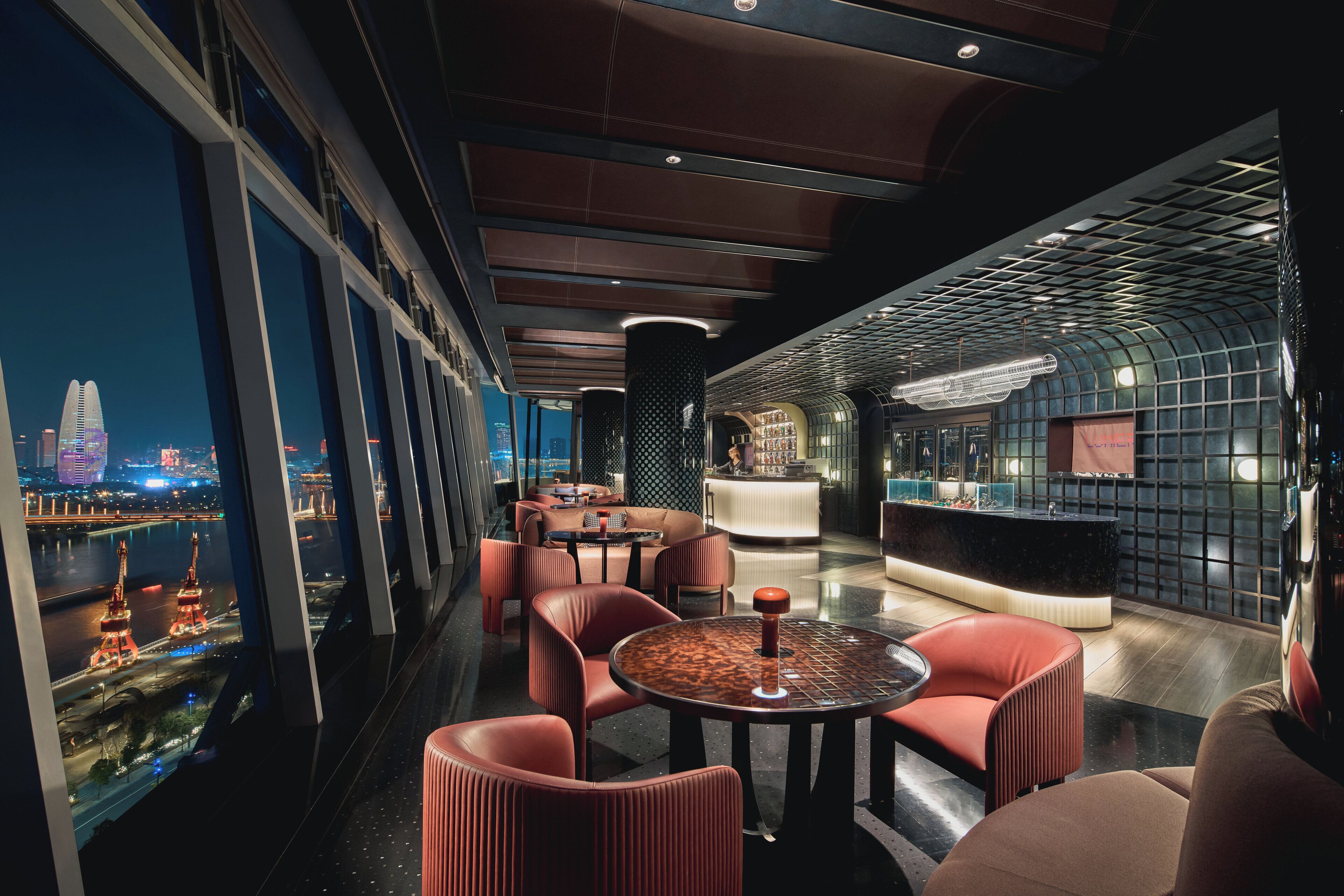 A modern lounge area with seating and a reception desk, large windows offering a view of a cityscape and a river.