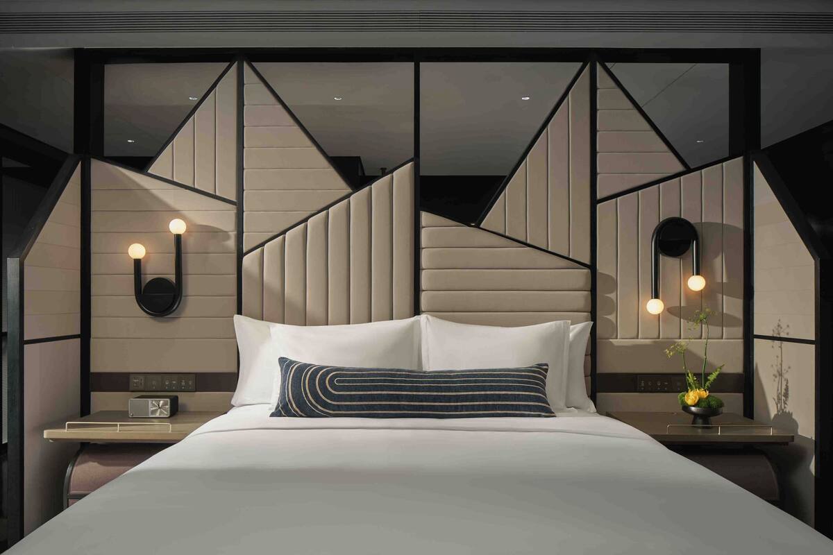 A modern hotel room with a large bed, a nightstand with a radio, and a wall-mounted mirror.