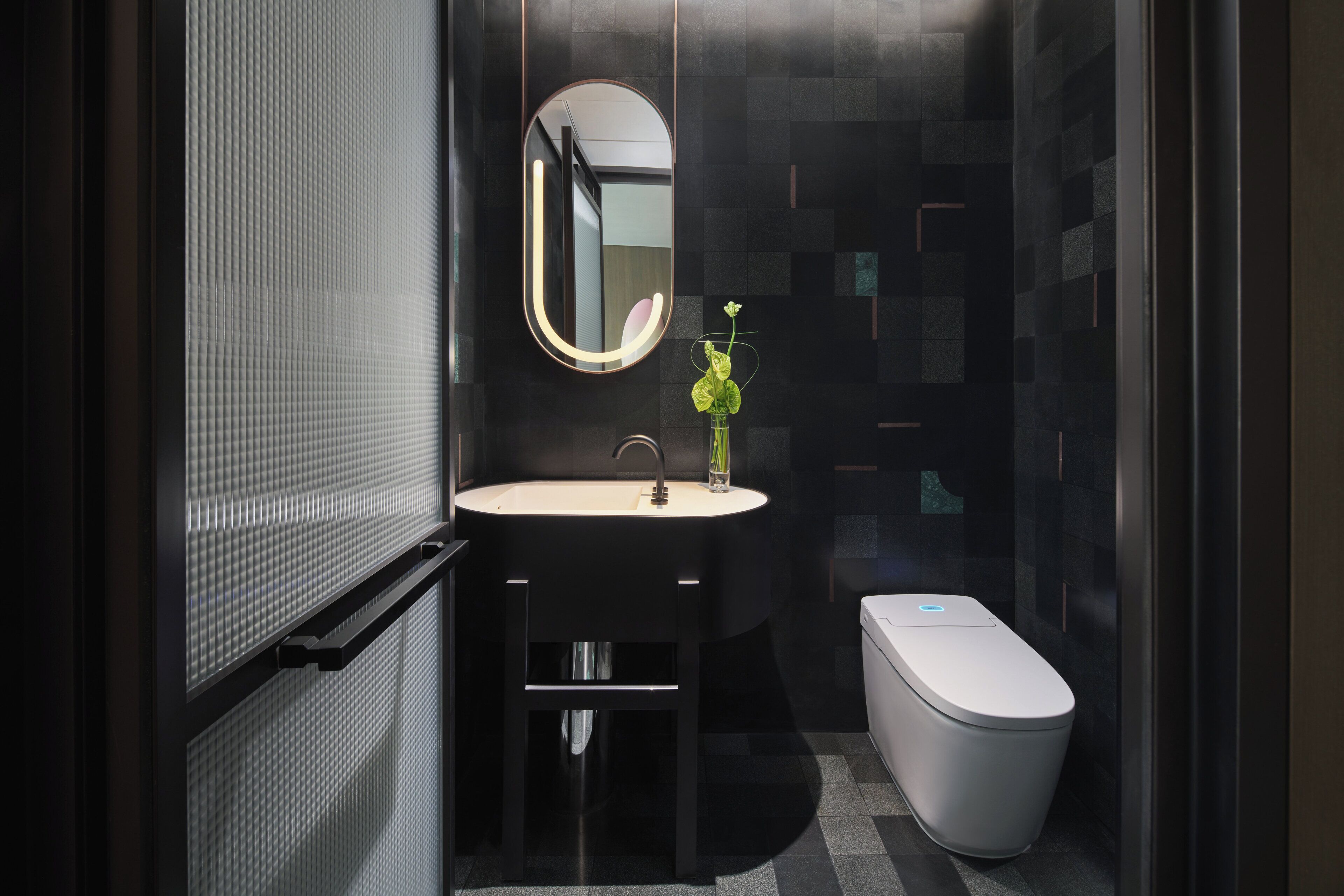 A modern bathroom with a round mirror, a sink, and a toilet.
